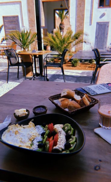 Healthy breakfast spread with scrambled eggs, fresh fruit chia bowl, sliced baguette basket, and coffee served on an outdoor patio table.